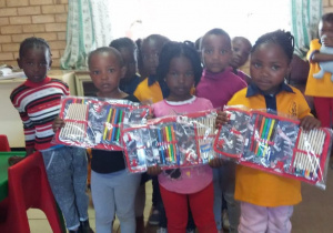 Zdjęcie przedstawia grupę dzieci z Afryki, które w rękach trzymają prezenty, piórniki z wyposarzeniem do szkoły.